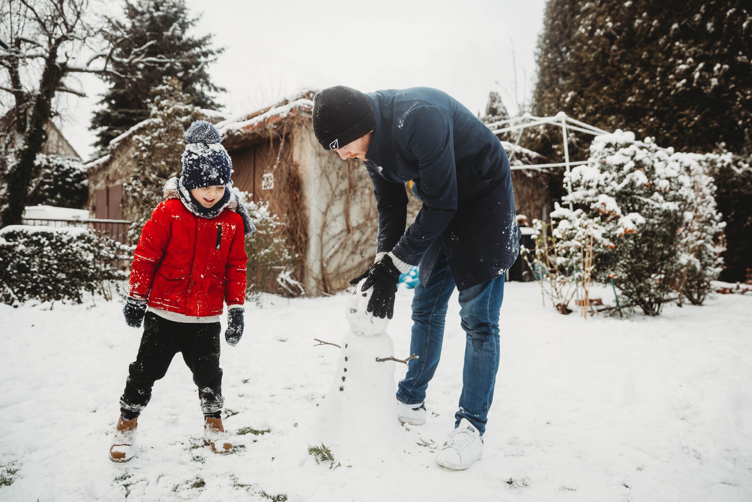 son and dad building snowman in garden