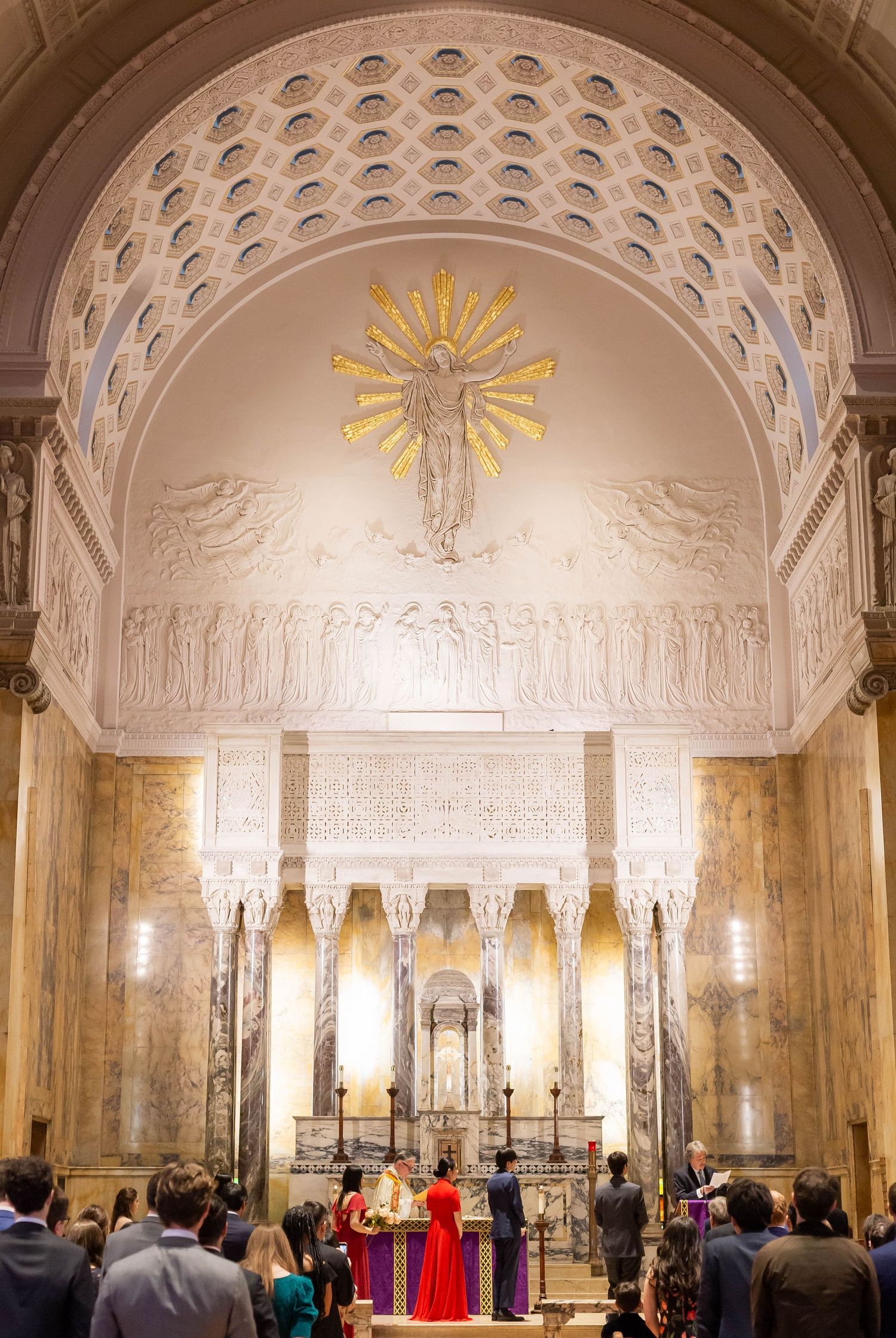 Ornate church interior with vaulted ceiling, golden sun rays, and marble columns during a ceremony.