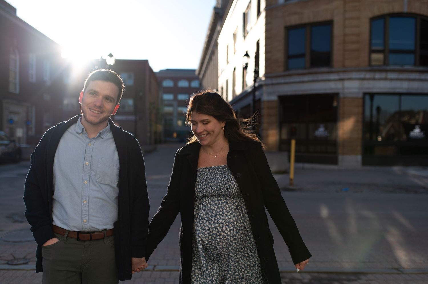 A couple walks together on a city street at sunset, with the woman wearing a polka dot dress and black cardigan.