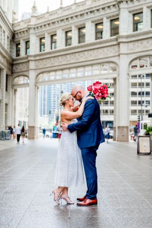 couple in navy suit and glittery dress with red bouquet walking under Wrigley building at Chicago Elopement
