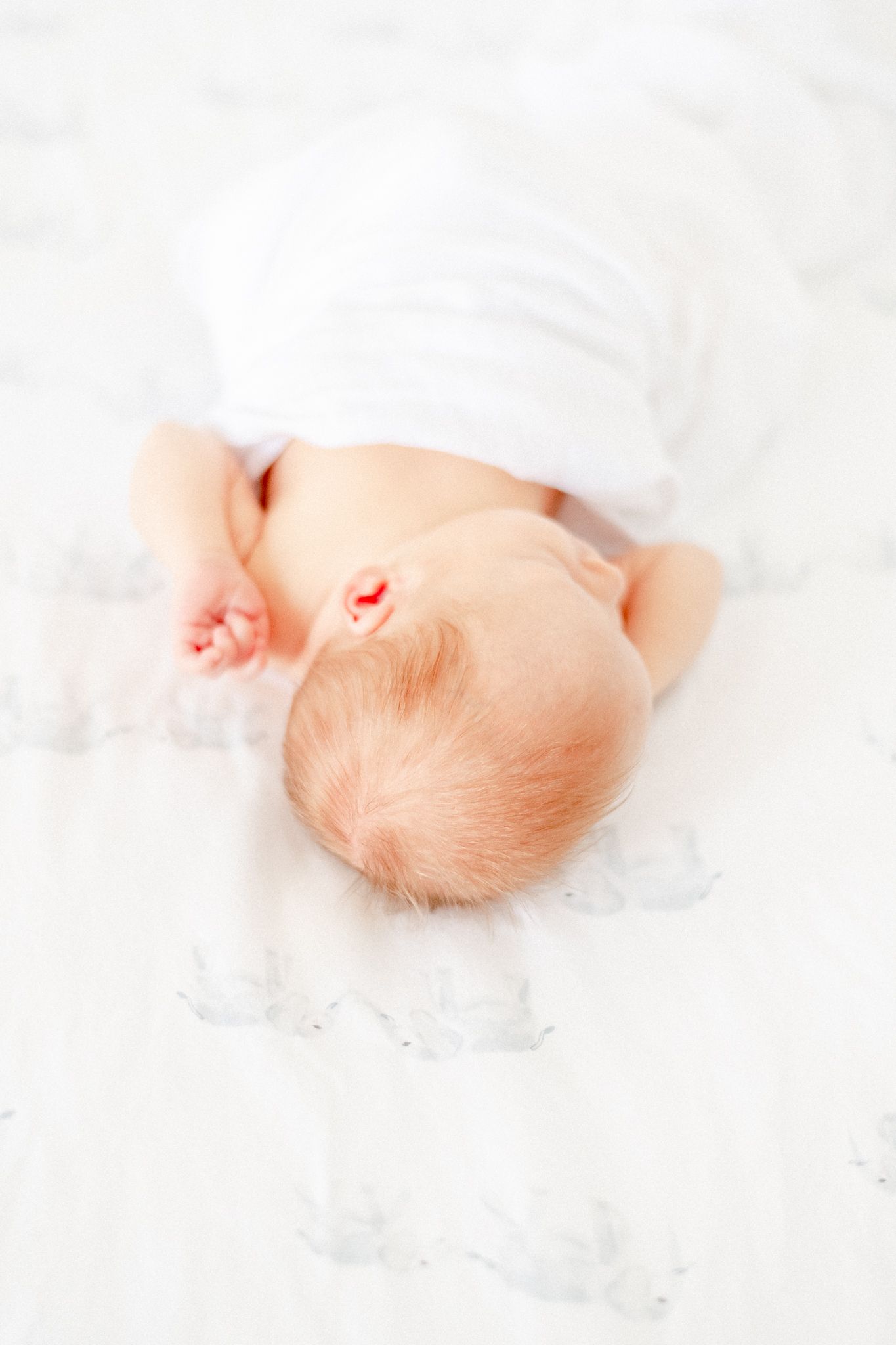 Red haired newborn baby asleep on her white and blue sheets