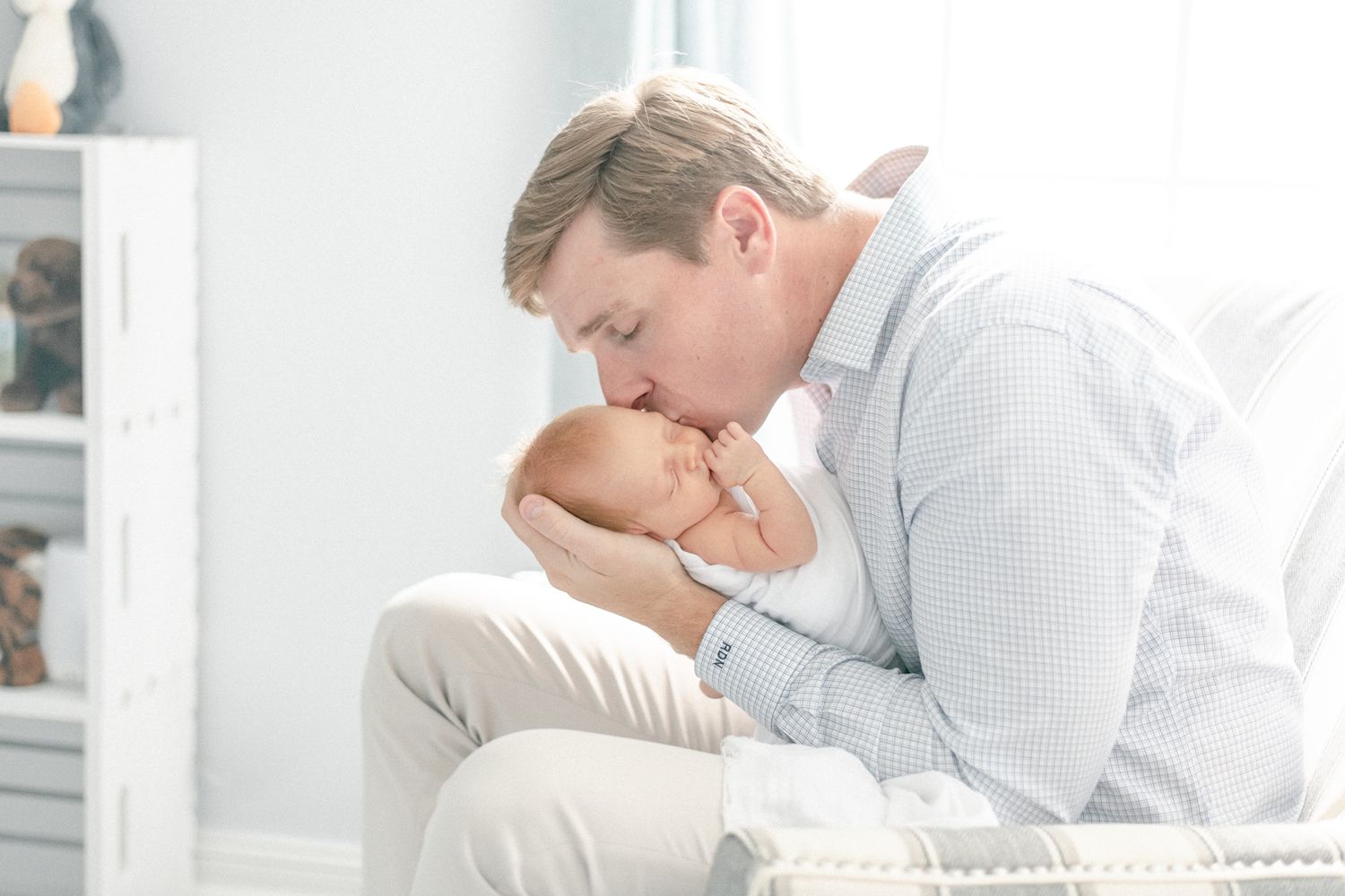 Father kisses newborn baby as he rocks her by the nursery window