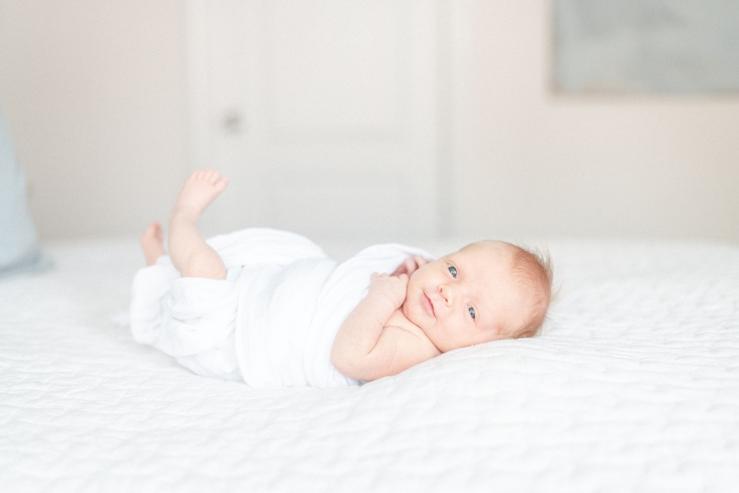 Newborn baby girl with red hair looks at camera with foot in the air