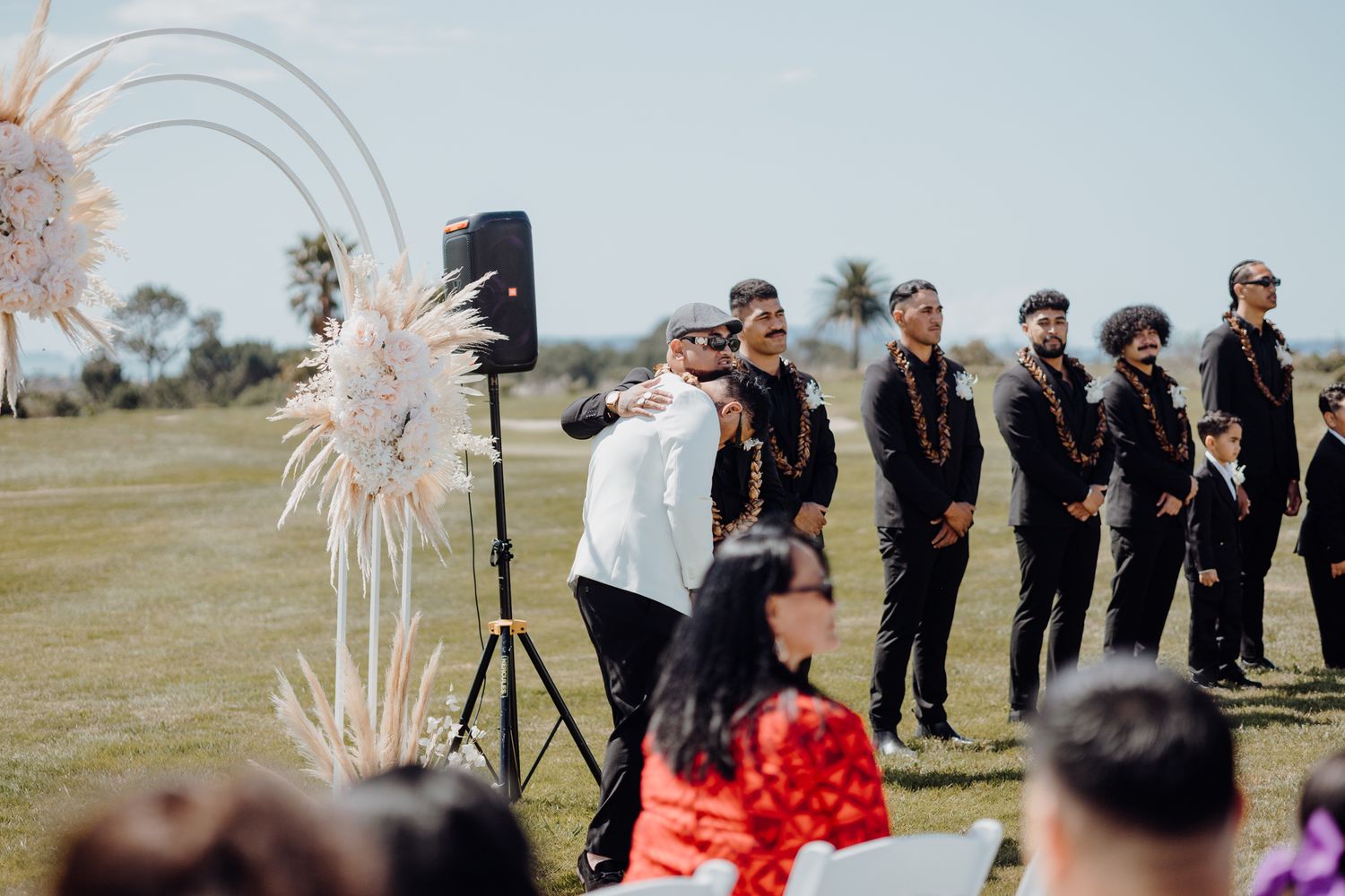 Wedding ceremony setup on a lawn with pampas grass decorations and palm trees in the background.