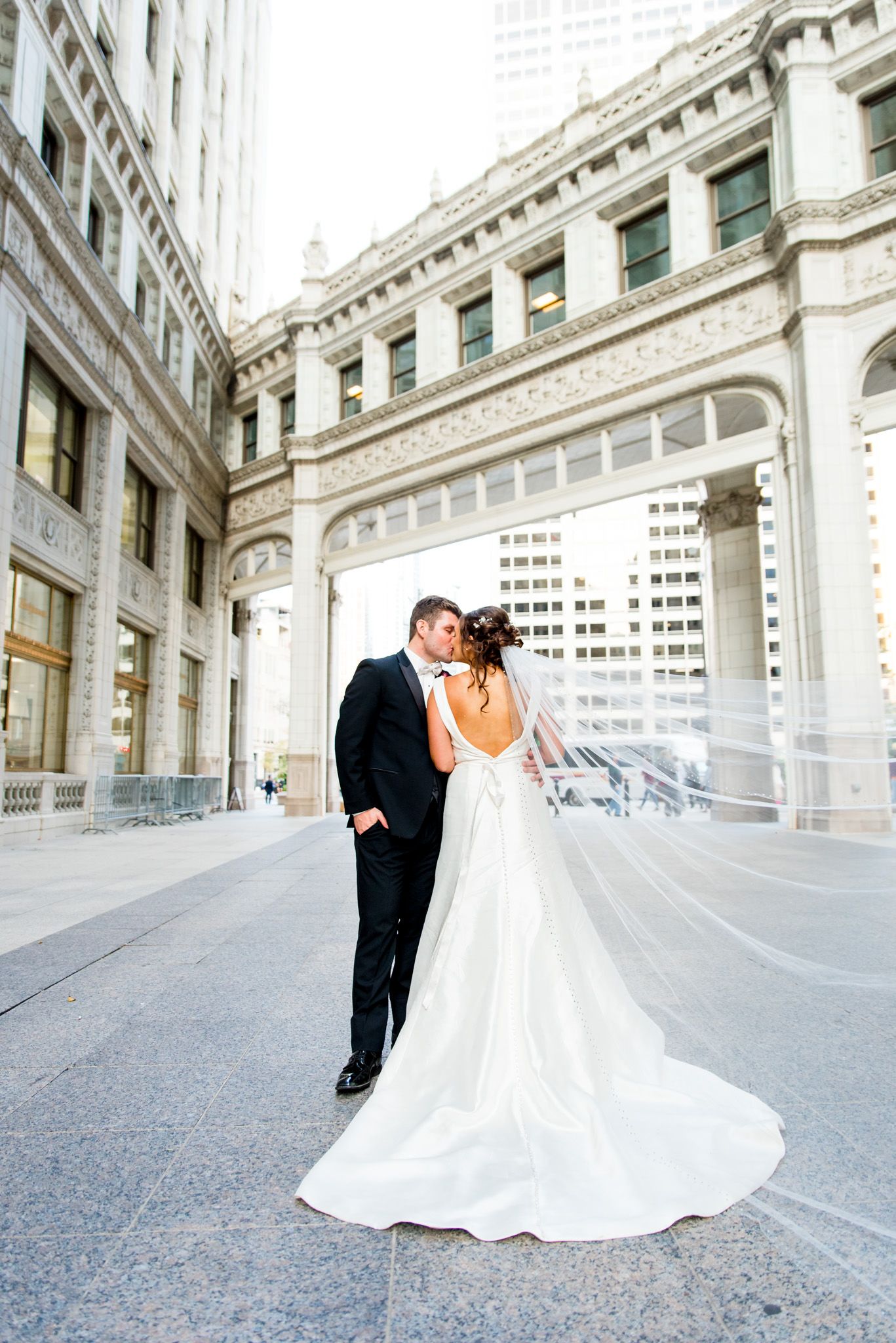 groom kisses bride and her veil flies in the streets of chicago at Wrigley Building