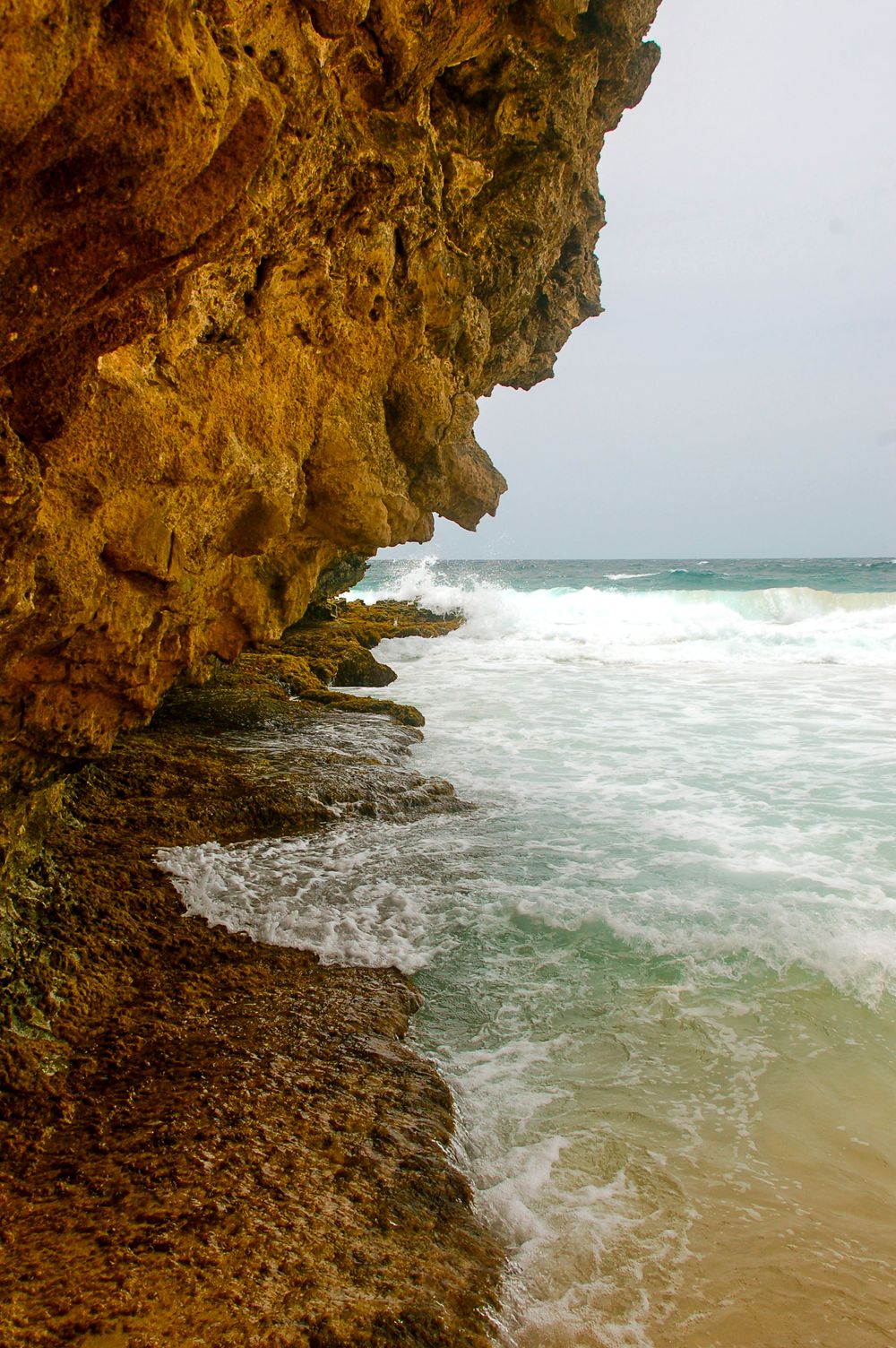 Weathered orange limestone cliff face meets turbulent ocean waves below.