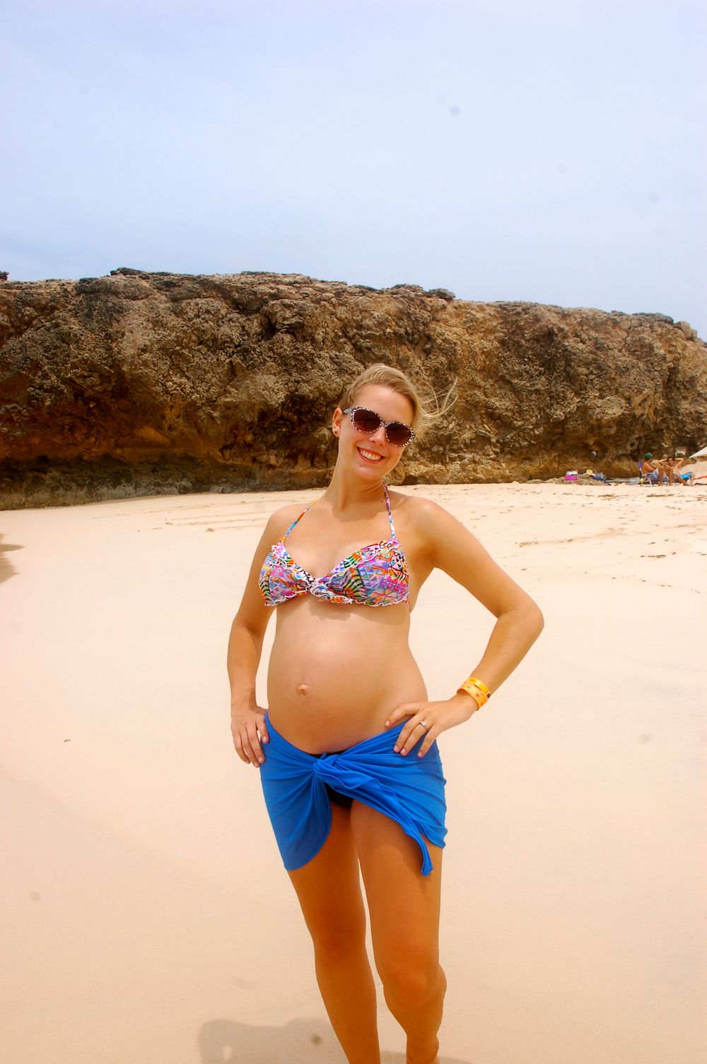 A beachgoer poses on sandy shore with dramatic rock formations in the background.