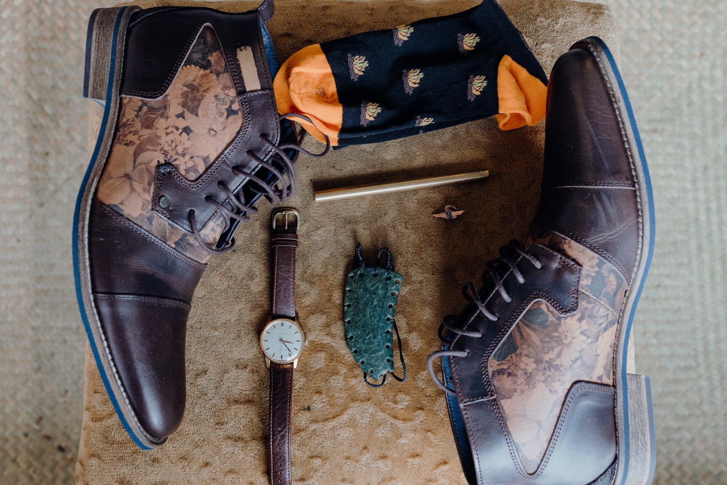 Groom's accessories including leather boots, patterned socks, and watch arranged on vintage surface.