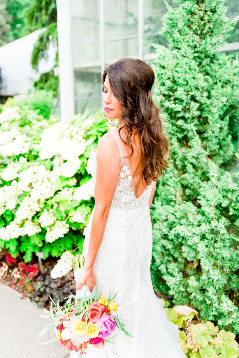 brown hair bride with loose curls and half up do holding bouquet in front of juniper tree at Krohn Conservatory