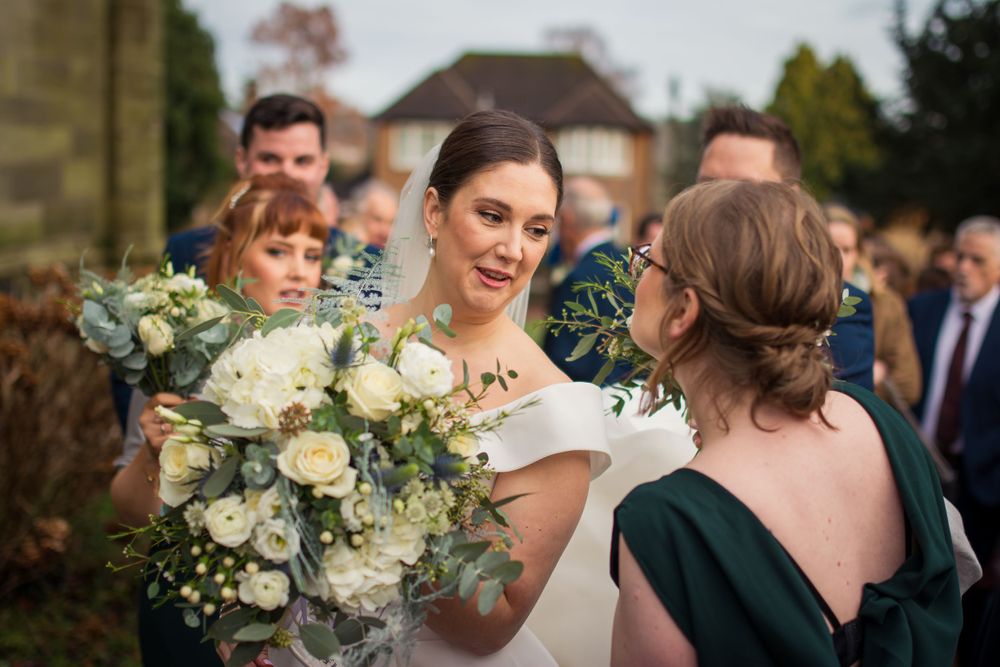 Wedding party gathers outdoors with elegant white floral bouquets and emerald green dresses.