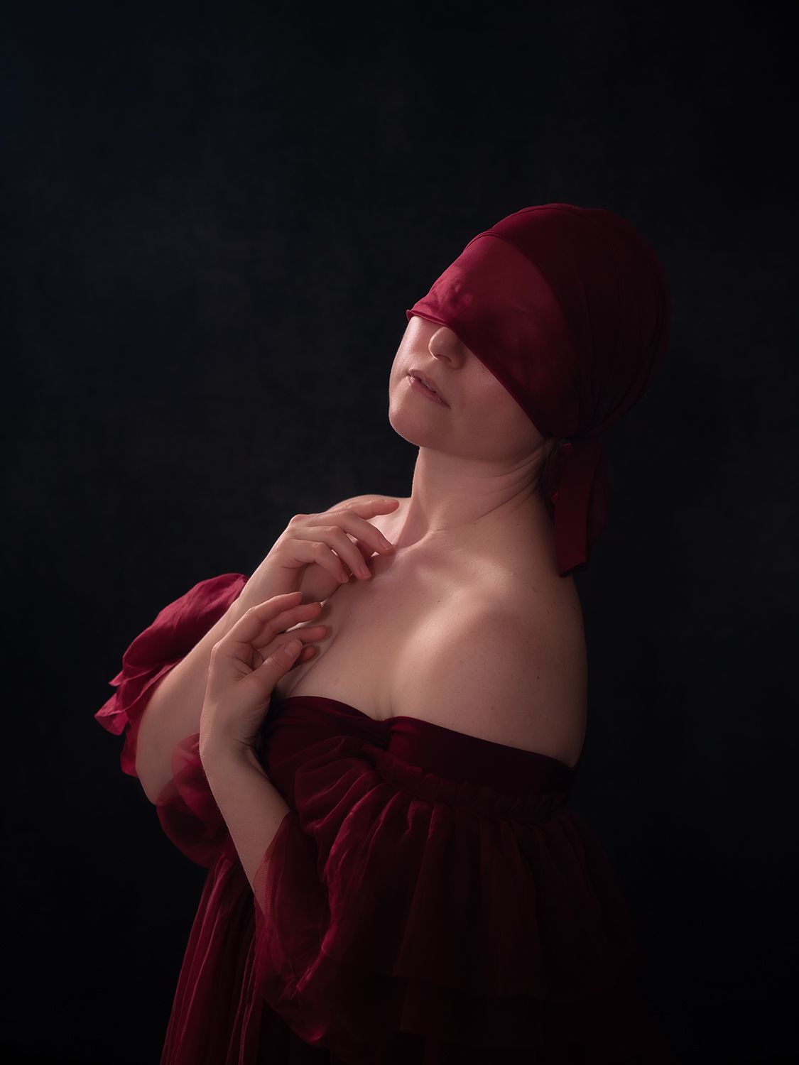Portrait of a young woman in a dark red tulle robe with a red sash covering her eyes, by Verity Thewlis, Oxfordshire.