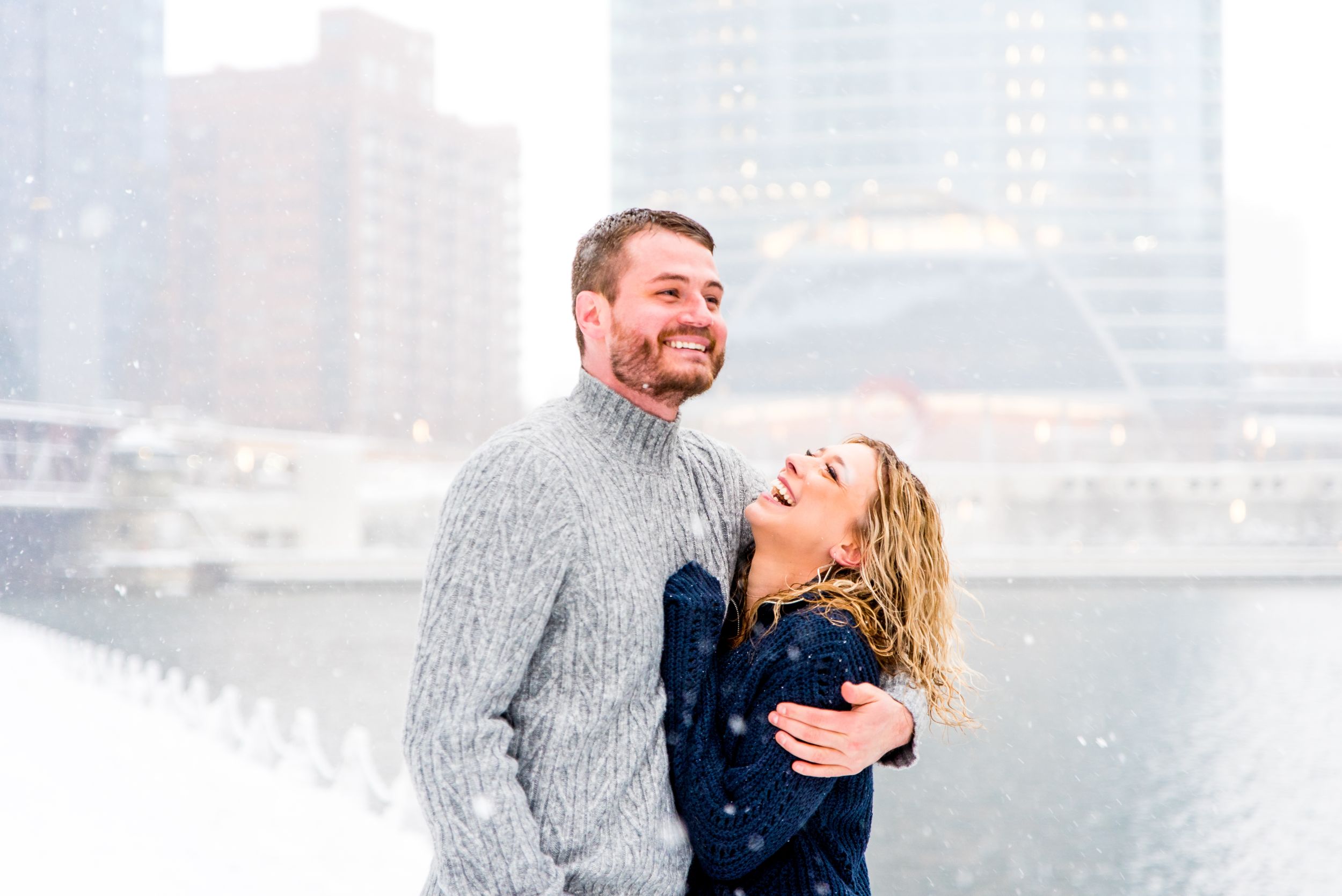 man and woman in navy and grey sweaters smiling in snow at Wolf Point Chicago