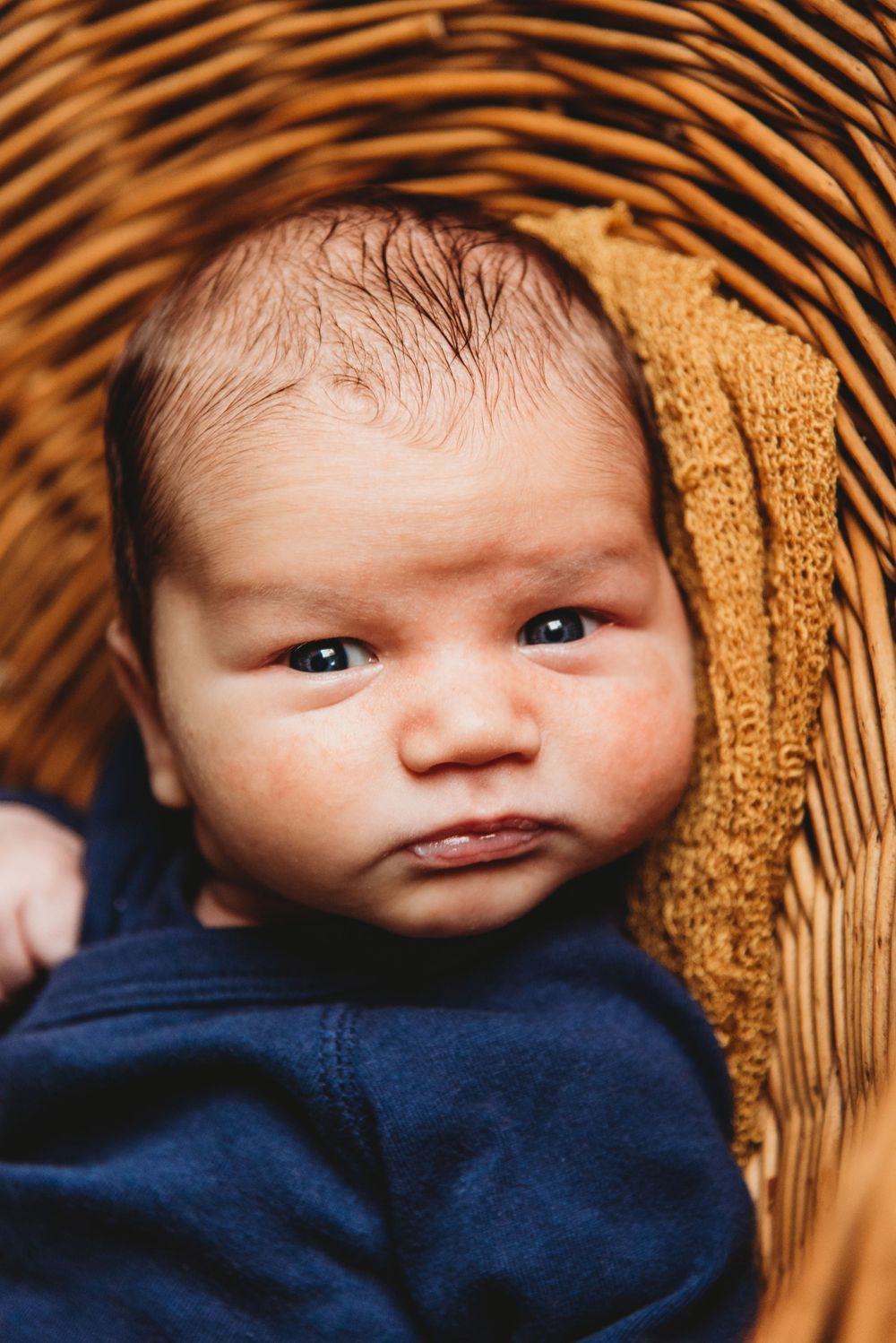 Baby in navy blue outfit rests in wicker basket with amber tones.