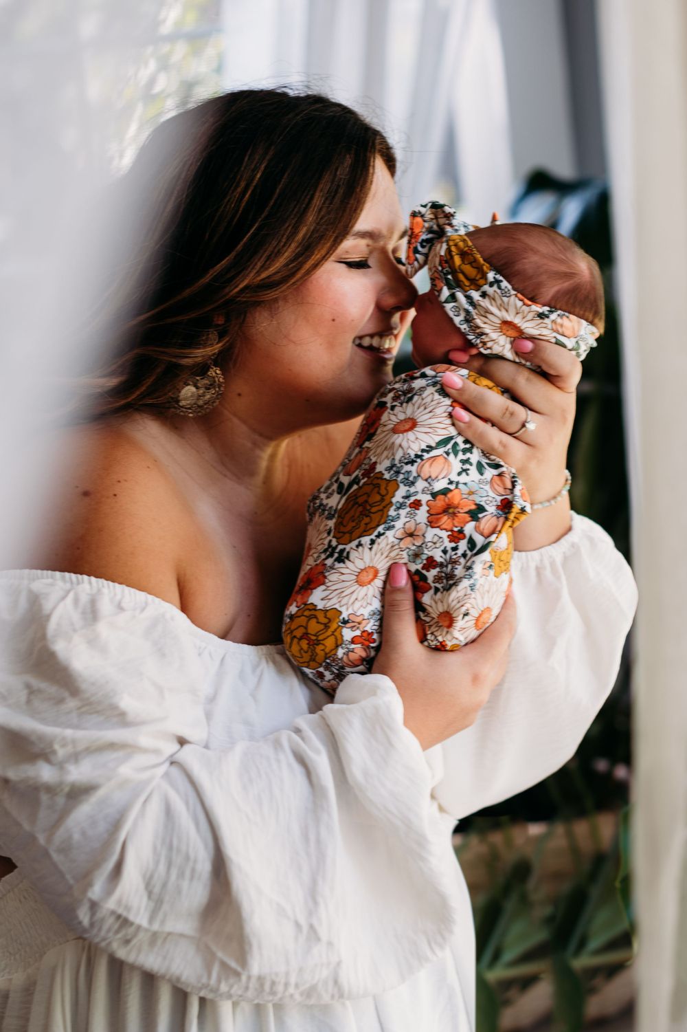 Intimate portrait of someone in a white dress holding a floral-wrapped bundle near a window.