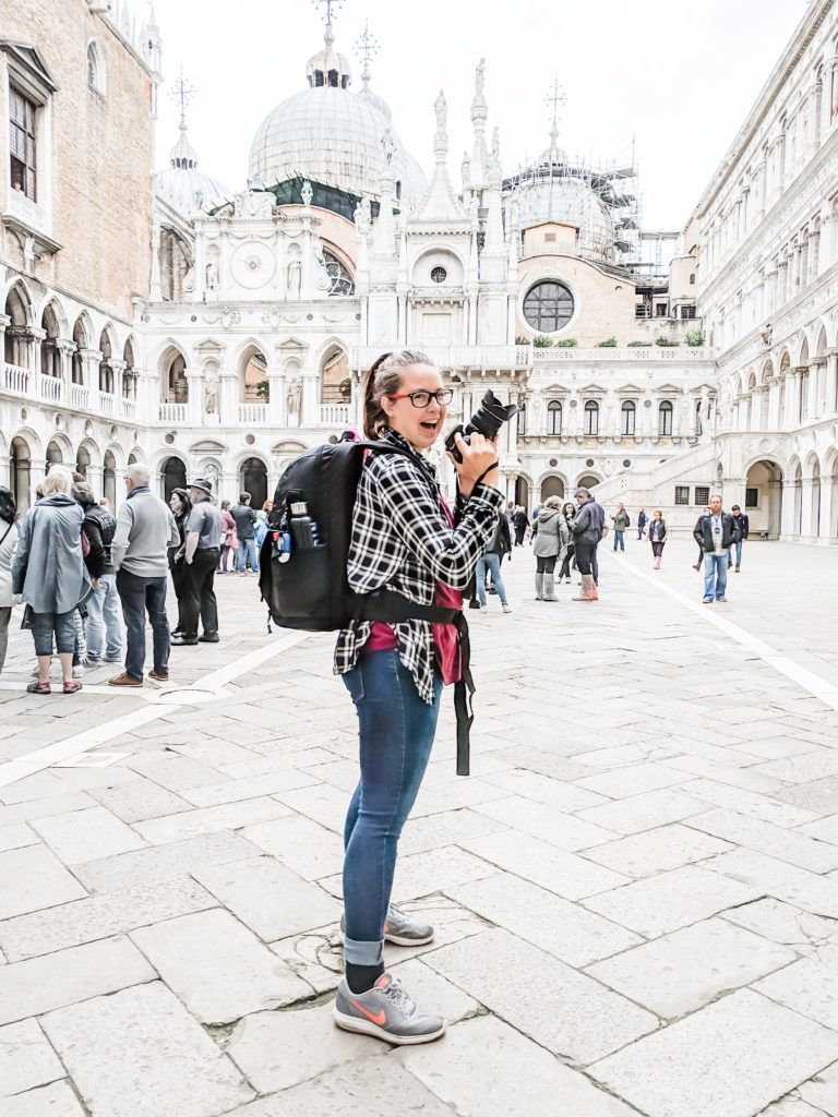 Woman standing with a backpack and camera in front of the Doge's Palace in Venice, Italy