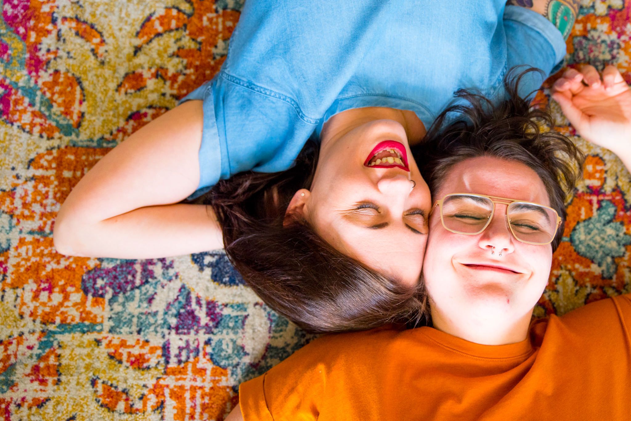 two woman laying on pink orange and blue rug with heads together, smiling