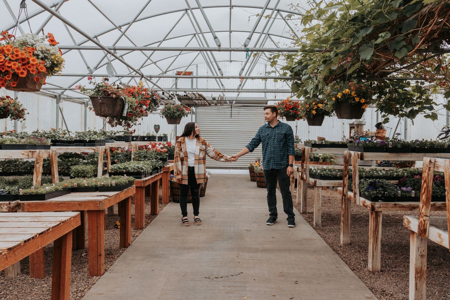 People walking through greenhouse with hanging planters and wooden tables.