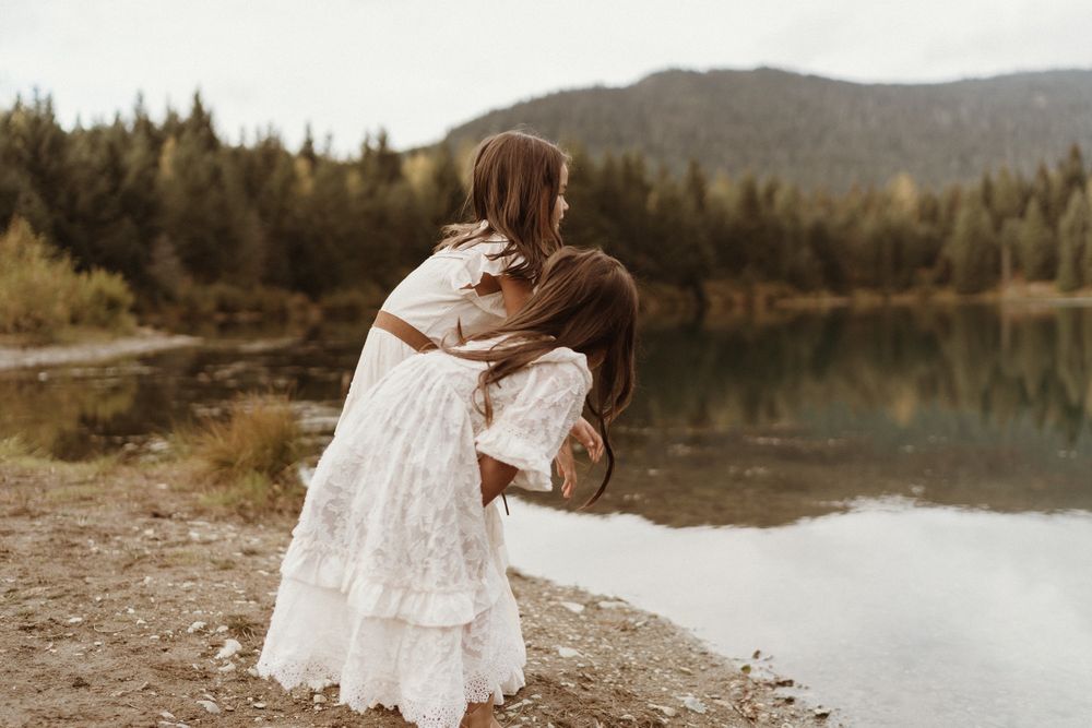 Little girls wearing white dresses peeking into lake water at Gold Creek Pond