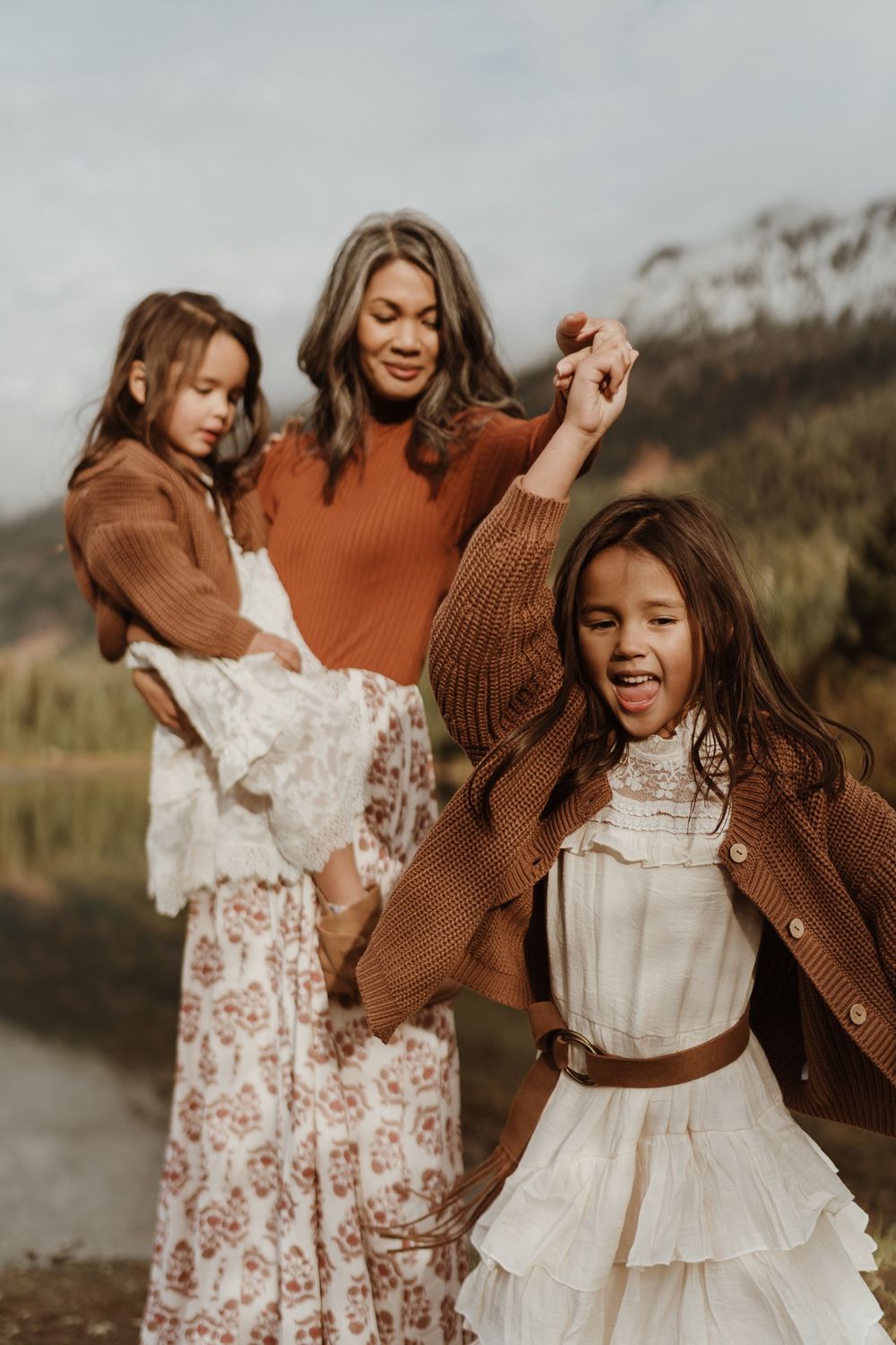 Mother twirling daughter while holding other daughter in arms at Gold Creek Pond