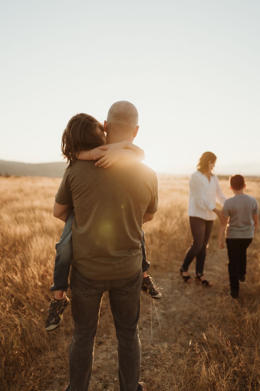 Father holding little boy with Mom and son in background in grassy field