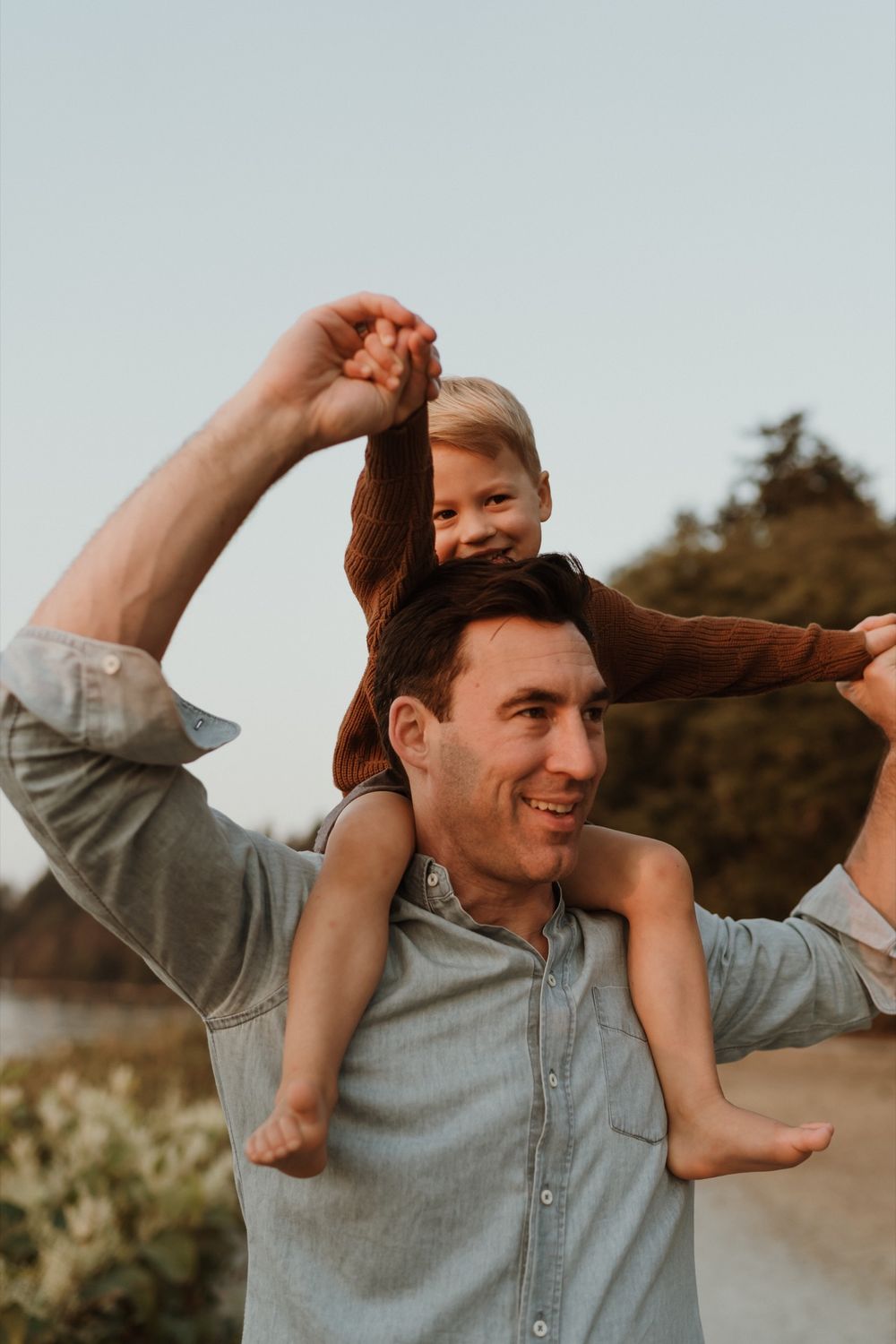 Dad wearing blue shirt giving little boy shoulder ride while holding his hands