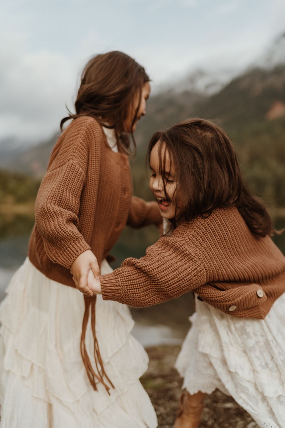 Little girls wearing white dresses and brown sweaters playing ring around the rosy