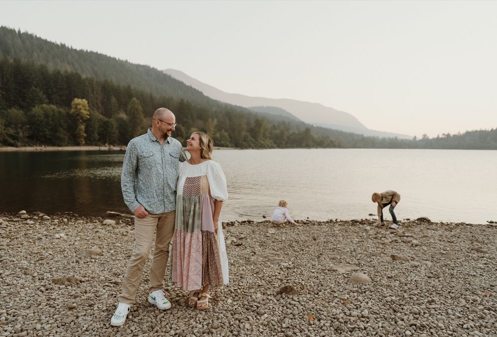 Mother and Father standing next to each other with little boys playing in lake in background at Rattlesnake Lake