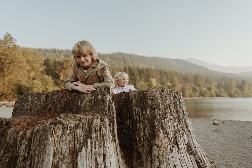 Little boy wearing brown blazer sitting in tree trunk with brother in background at Rattlesnake Lake