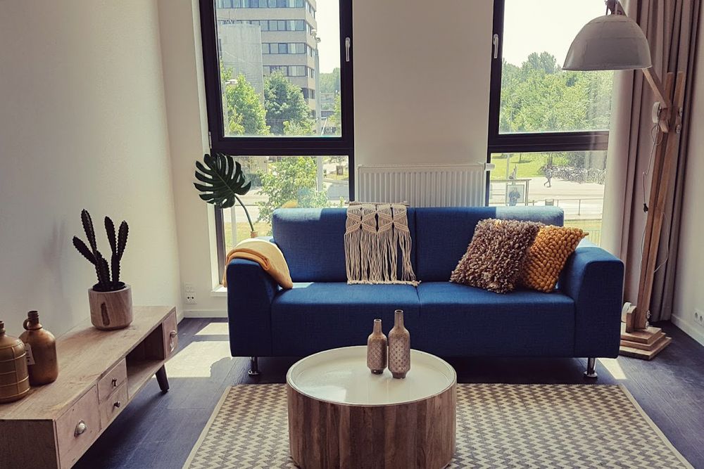 Studentenwoning met blauwe bank, kleed, staande lamp, kastje, ronde tafel en decoratie