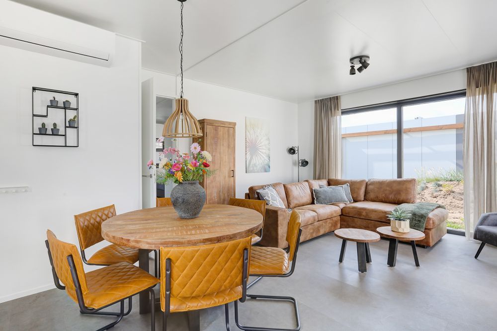 Woning met laungebank, ronde salontafeltjes, een ronde eettafel met zes stoelen en een stenen vaas met een veldboeket