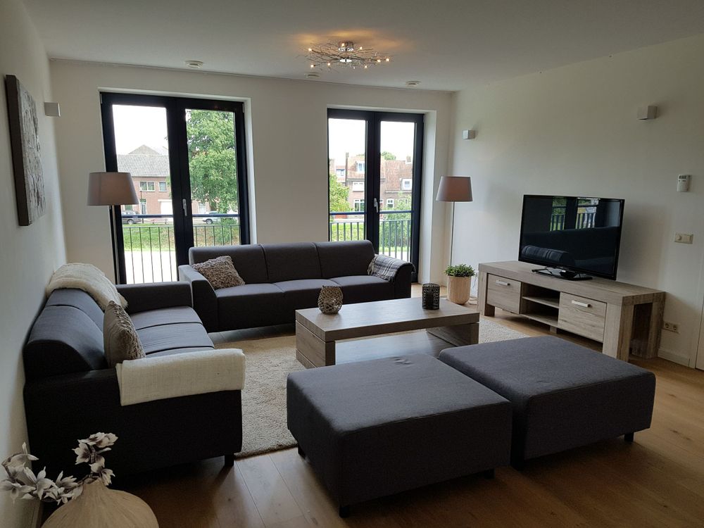 Woonkamer met bankstel en twee hockers, Tv-kastje en matchende salontafel, twee staande lampen en kussens en deco