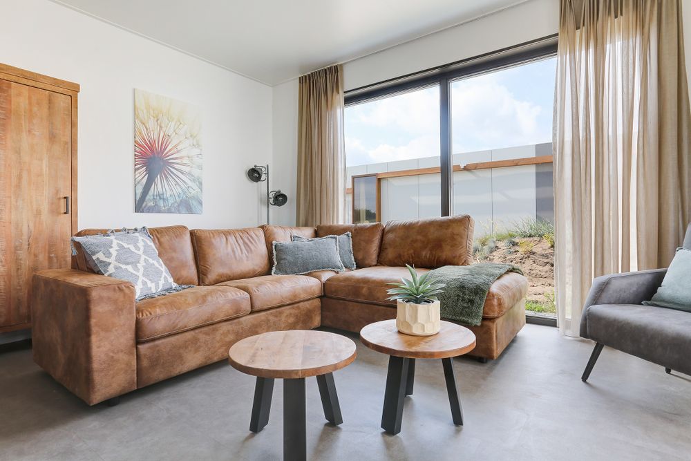 Bruine hoekbank en grijze fauteuil bij twee ronde salontafeltjes met plant in pot en decoratie
