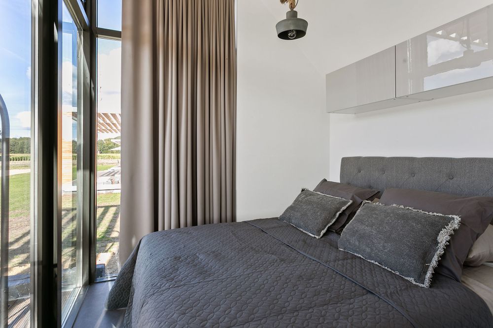 Luze boxpring grijs met vier kussens en sprei in een kamer met vrij uitzicht