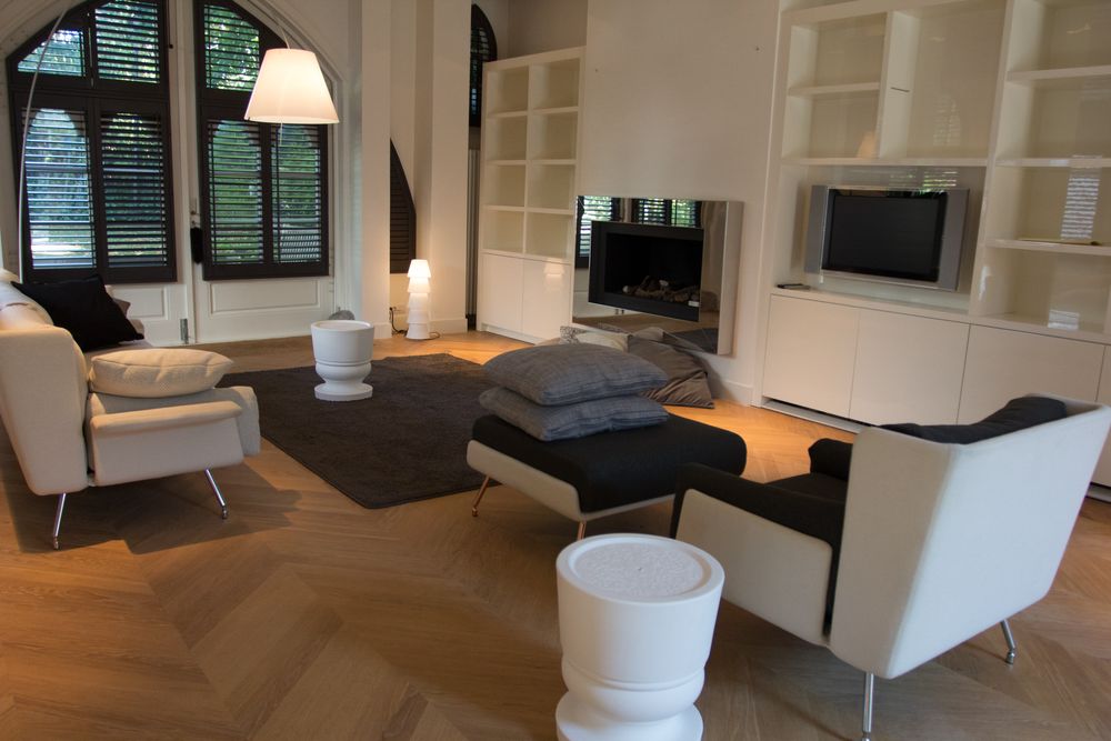 Huiskamer met witte bank, zwart-witte fauteuil en hocker, witte ronde bijzettafeltjes, designlampen en veel kussens