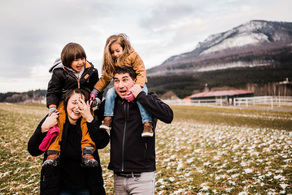Mother and father carrying son and daughter in shoulders in winter coats in Austrian mountains