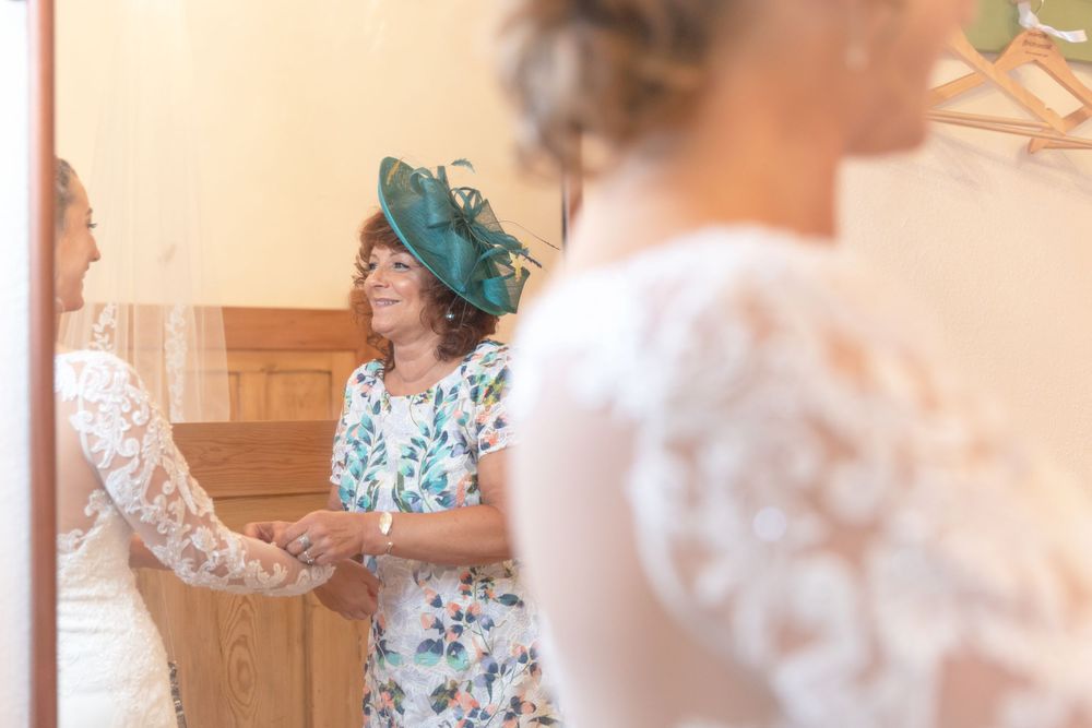 mother of the bride in hat helping her daughter, the bride to get dressed. Bridal preparation. Wedding goals.