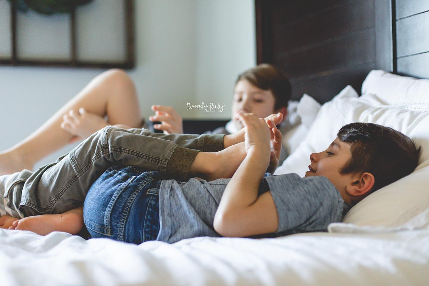 brother tickling his younger brother's toes while hanging out on parent's bed