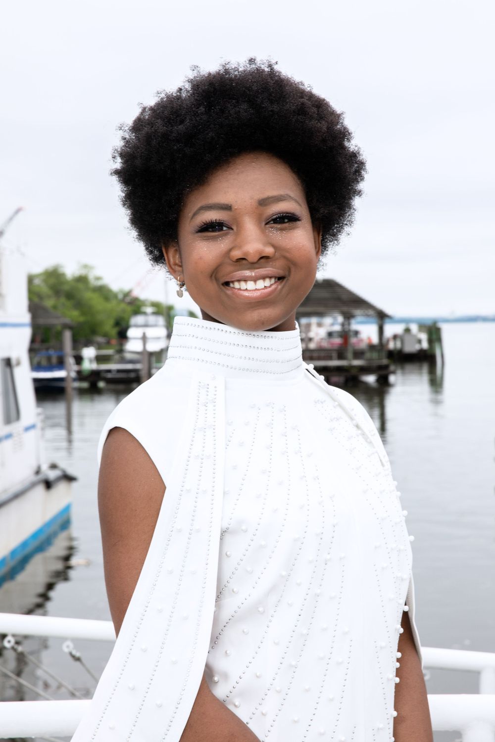 Someone wearing an elegant white turtleneck top poses by the water at a marina.