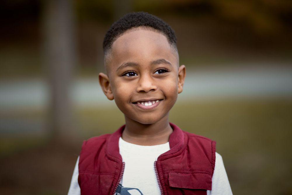 Child wearing a burgundy vest and white t-shirt smiles brightly at the camera.