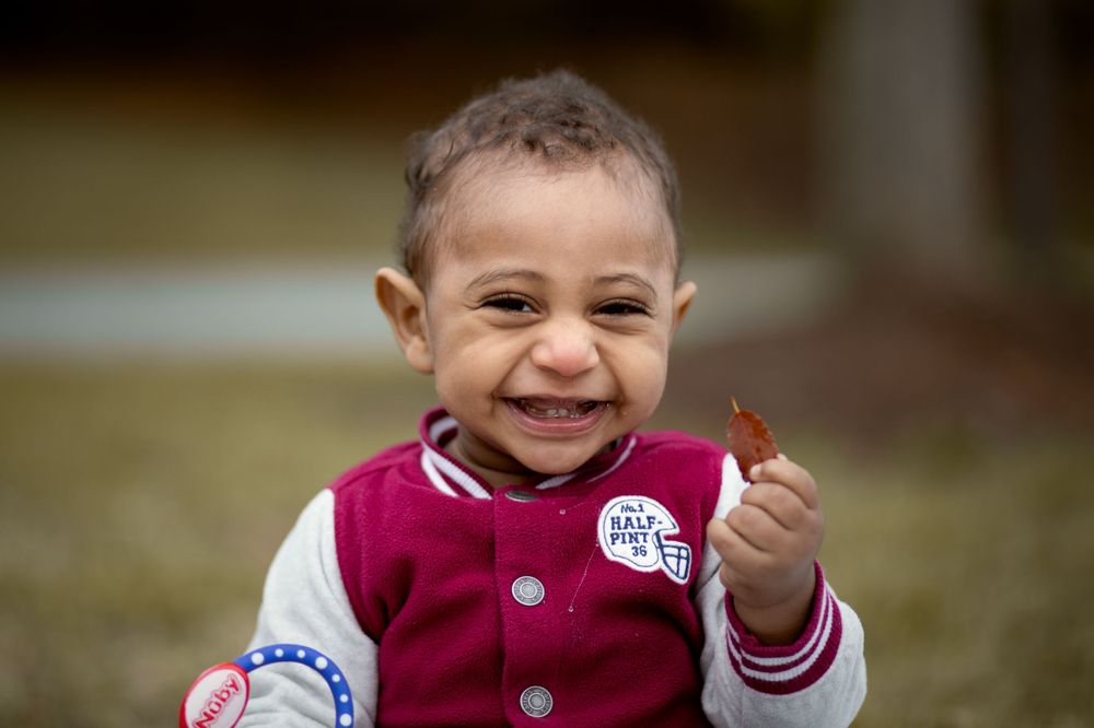 Young child in a burgundy jacket smiles while holding something small.