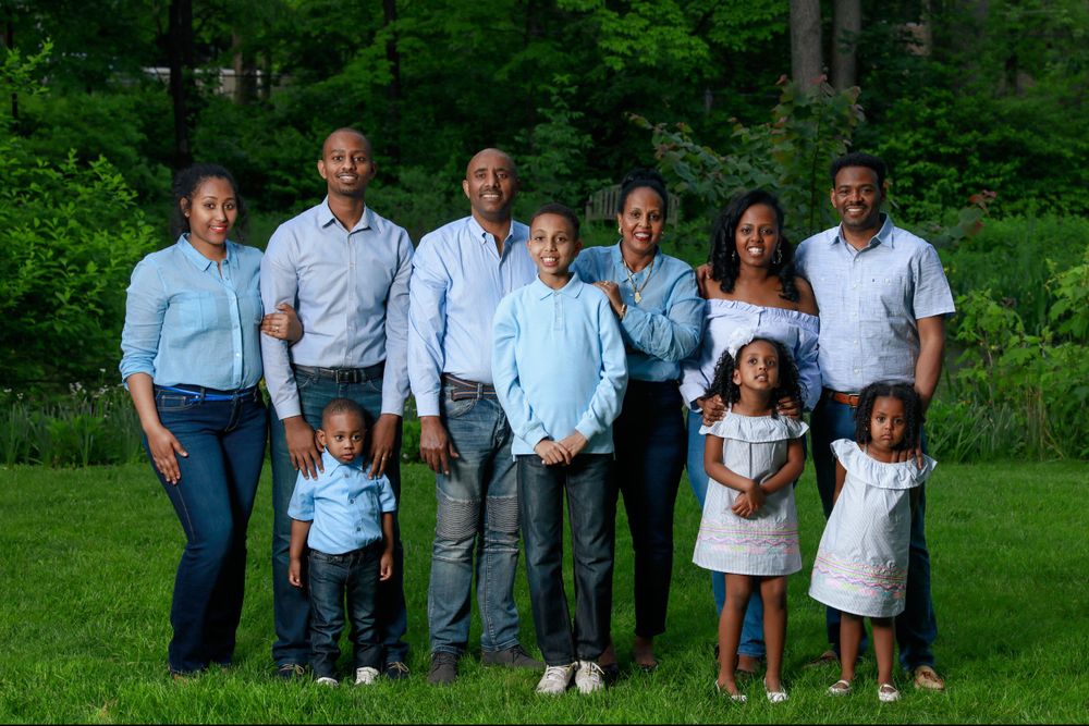 A multi-generational family in coordinated blue and white outfits poses together outdoors.