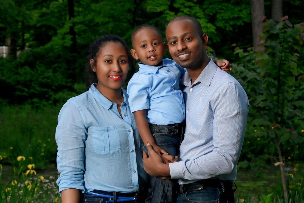 A happy family in coordinated blue outfits poses together in a lush green forest setting.