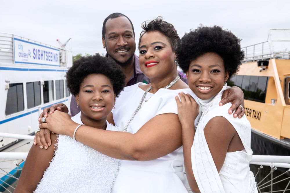 A happy family in white outfits smiles and hugs while posing at a marina.