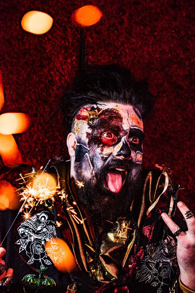 Theatrical portrait with face paint and sparklers against orange bokeh lights.