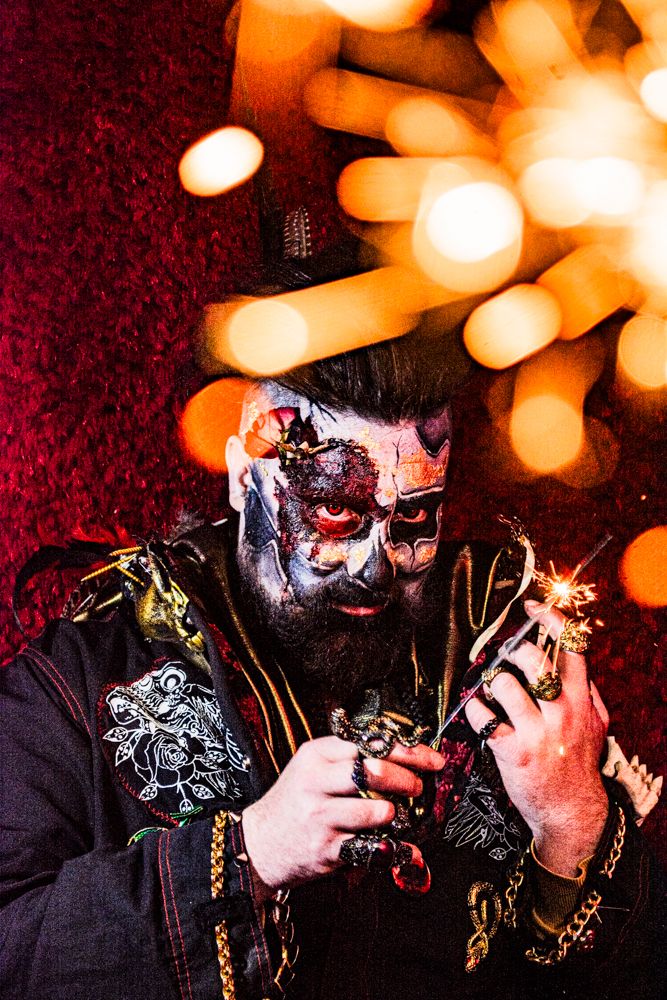 Figure with face paint poses with sparklers against bokeh light effects.