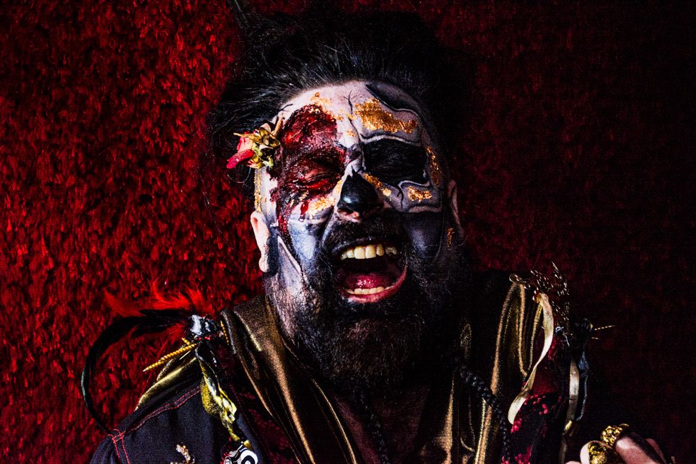 Dramatic portrait with elaborate face paint against dark red background.