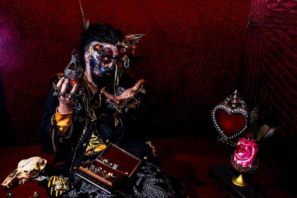 Gothic figure poses with mechanical props and heart decoration against red backdrop.