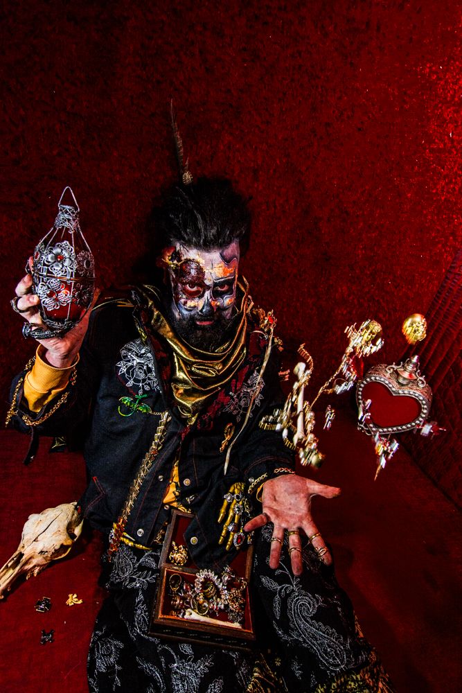 Steampunk styled figure poses with mechanical props against crimson background.