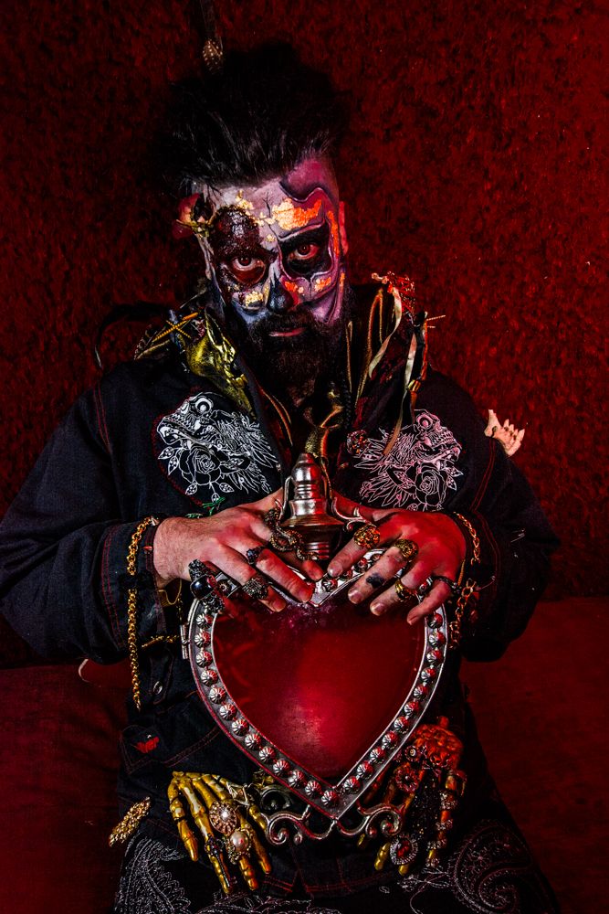 Gothic figure holds ornate heart-shaped prop while wearing elaborate costume.