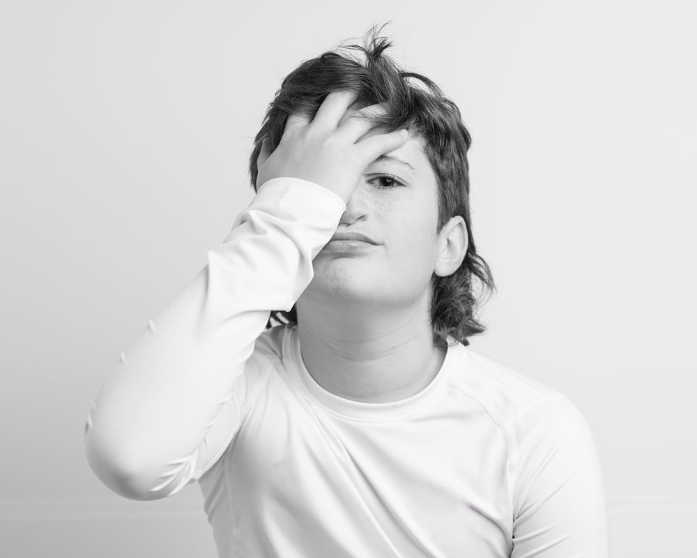 Black and white portrait of someone in white shirt with hand covering face at home studio i